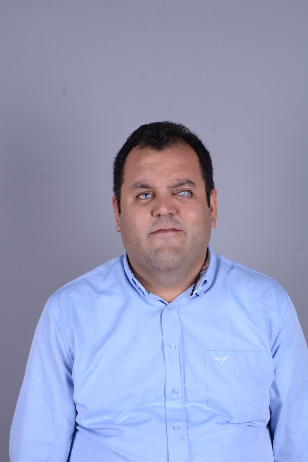 Açık mavi gömlek giymiş Oğuz Özdemir’in, sade gri bir arka plan önünde yakından çekilmiş görüntüsü